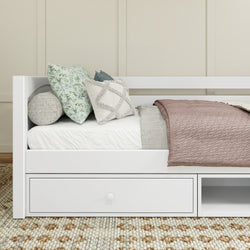 Stylish white daybed with storage drawer, decorated with mixed patterned pillows and a cozy blanket, in a minimalist bedroom setting.