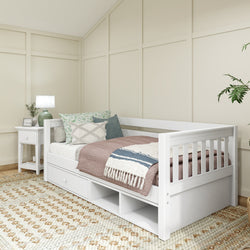 White wooden daybed with storage drawers, cozy pillows, and a throw blanket in a modern bedroom with beige walls and a geometric-patterned rug.