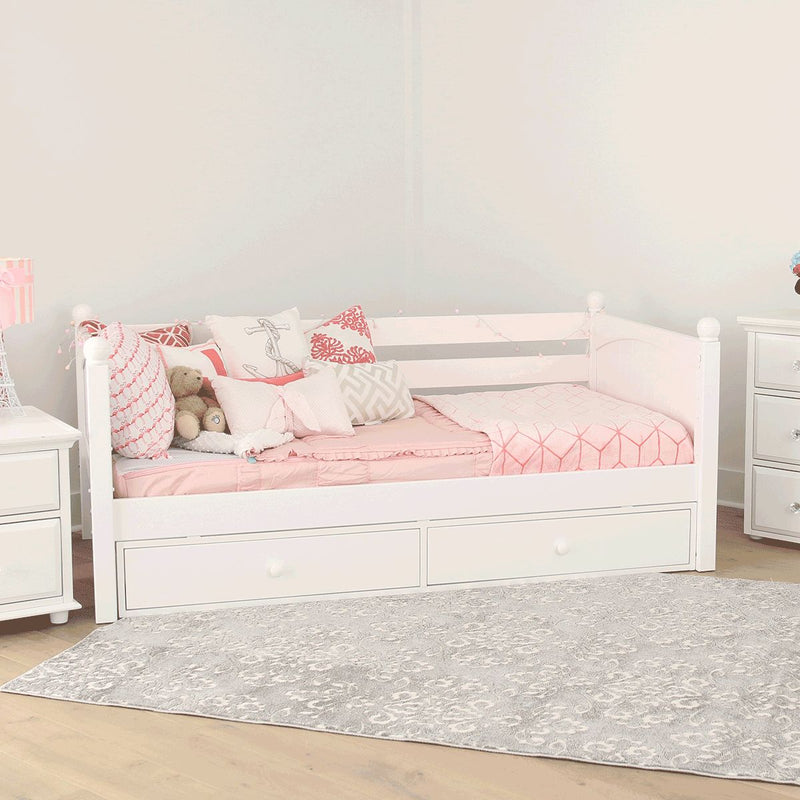 White wooden daybed with built-in storage drawers, pink quilted bedding, decorative throw pillows and teddy bear in a bright girls' bedroom with white nightstands and gray patterned rug