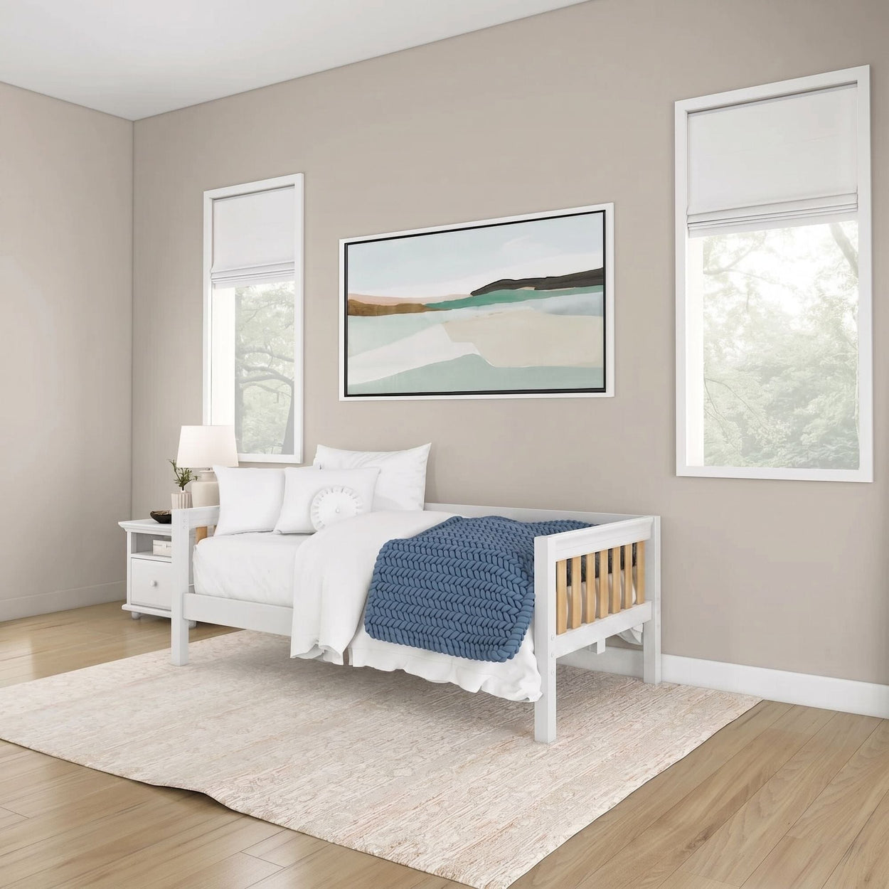 Modern minimalist bedroom with white daybed, blue chunky knit blanket and white pillows, nightstand with lamp, framed abstract landscape art, white Roman shades, beige walls and light wood floor