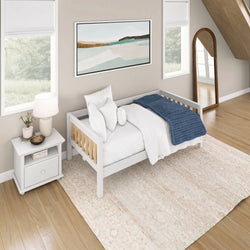 Sunlit minimalist bedroom with white wooden daybed, cozy blue chunky knit throw, white pillows, bedside lamp and nightstand, abstract wall art, arched mirror and hardwood floors