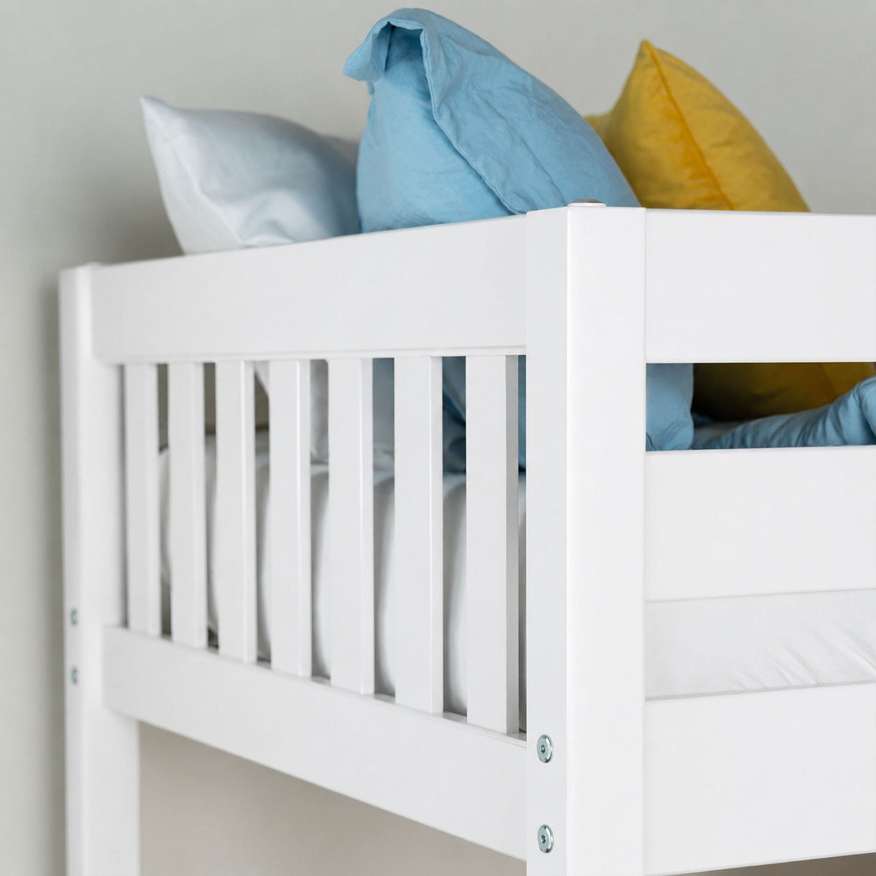 White wooden crib rail with light blue, yellow, and white pillows in a modern baby nursery.