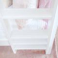 White slatted wooden ladder shelf with pastel pink and white muslin blankets draped over quilted bedding — minimalist baby nursery decor