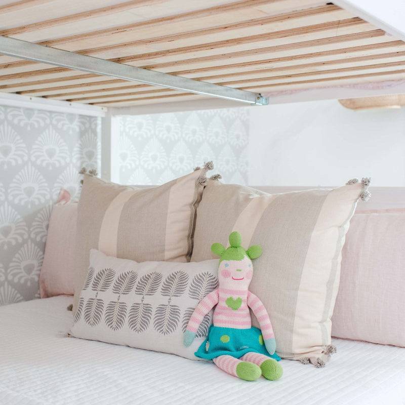 Pastel kids bedroom with wooden bunk bed slats, neutral striped pillows, patterned wallpaper, and a knitted doll on soft bedding