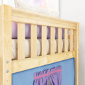 Close-up of a natural light-wood bunk bed guardrail with vertical slats, knit blanket and purple pillow against a blue fabric panel — children's loft bed detail