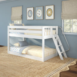 White wooden twin-over-twin bunk bed with ladder and metal slide in a light-blue kids' bedroom, yellow-striped bedding, celestial wall art, beige Roman shades, and natural jute rug