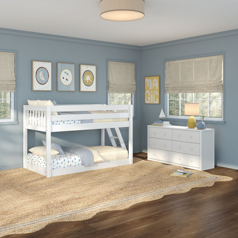 Modern children's bedroom with white bunk bed, blue walls, framed artwork, white dresser, table lamp, windows, and woven jute rug