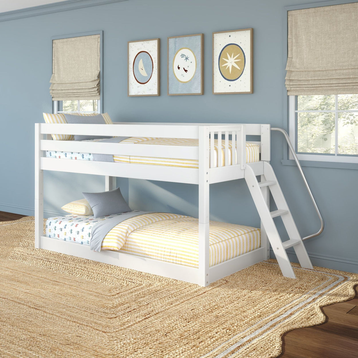 Modern white wooden twin-over-twin bunk bed with angled ladder in a coastal blue kids' bedroom, yellow-striped bedding, moon-and-star framed art, large windows, and natural jute area rug