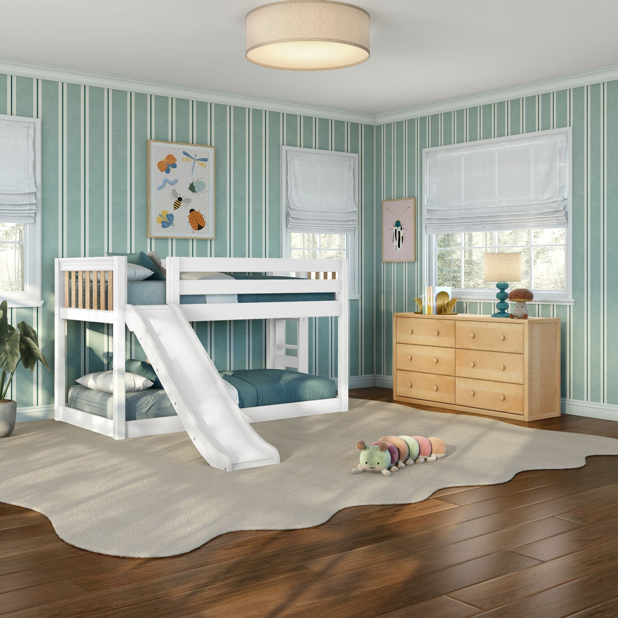 Sunlit kids' bedroom featuring a white bunk bed with slide, teal striped wallpaper, light wood dresser, and plush caterpillar toy