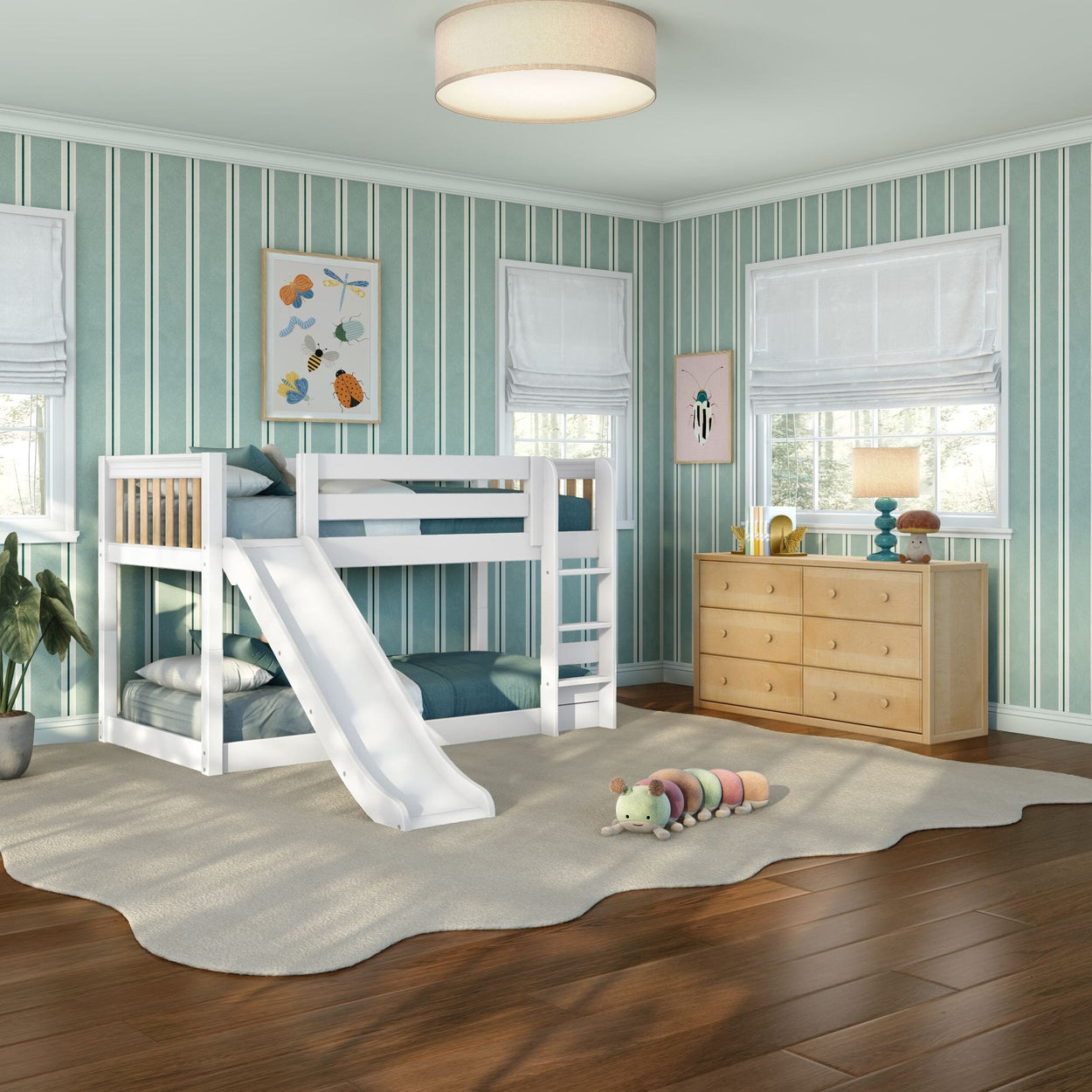 White kids bunk bed with slide in a bright children's bedroom with teal striped wallpaper, wooden dresser, hardwood floors, soft cream rug and plush caterpillar toy