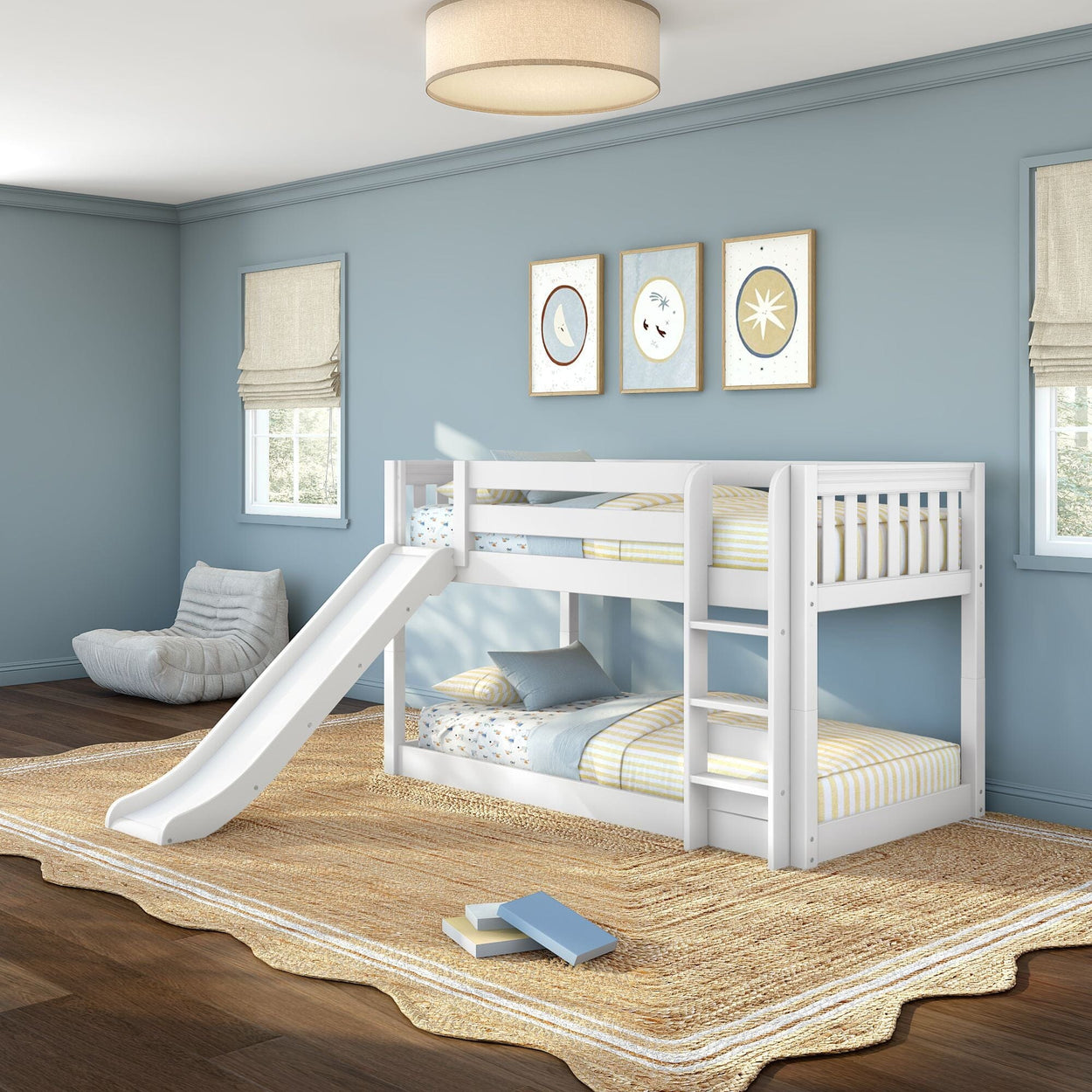 White kids bunk bed with slide in a modern blue bedroom, ladder, striped bedding, natural jute rug and framed wall art