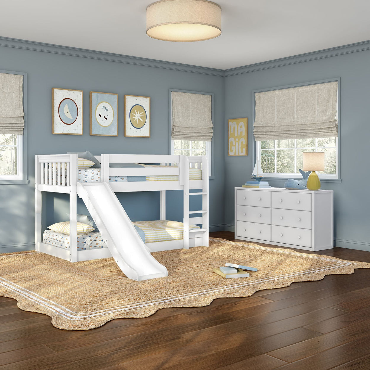 White twin-over-twin bunk bed with slide in a light-blue children's bedroom featuring framed wall art, beige Roman shades, white dresser with lamp and nautical decor, woven jute rug and hardwood floors