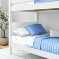 White twin wooden bunk bed with blue quilted comforter, star-print white sheets and pillows in a modern kids' bedroom with potted plant