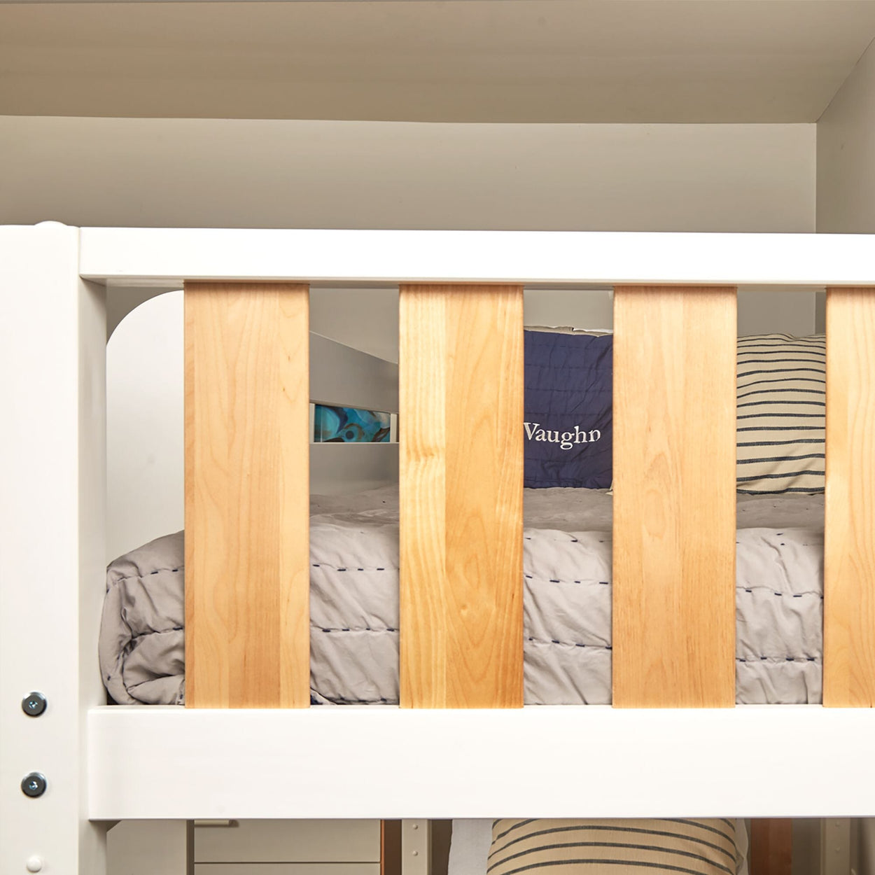 Close-up of white and natural wood bunk bed with gray quilt and striped pillows in a modern kids' bedroom