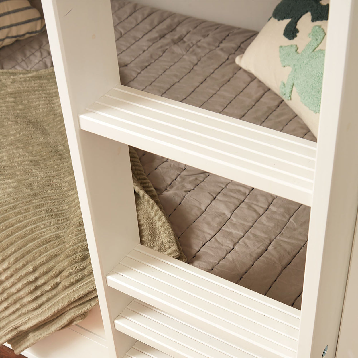 White wooden bunk bed ladder next to cozy beige quilted bedding with green decorative pillow.