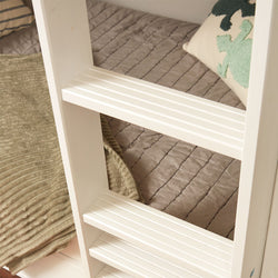 White wooden bunk bed ladder next to cozy beige quilted bedding with green decorative pillow.