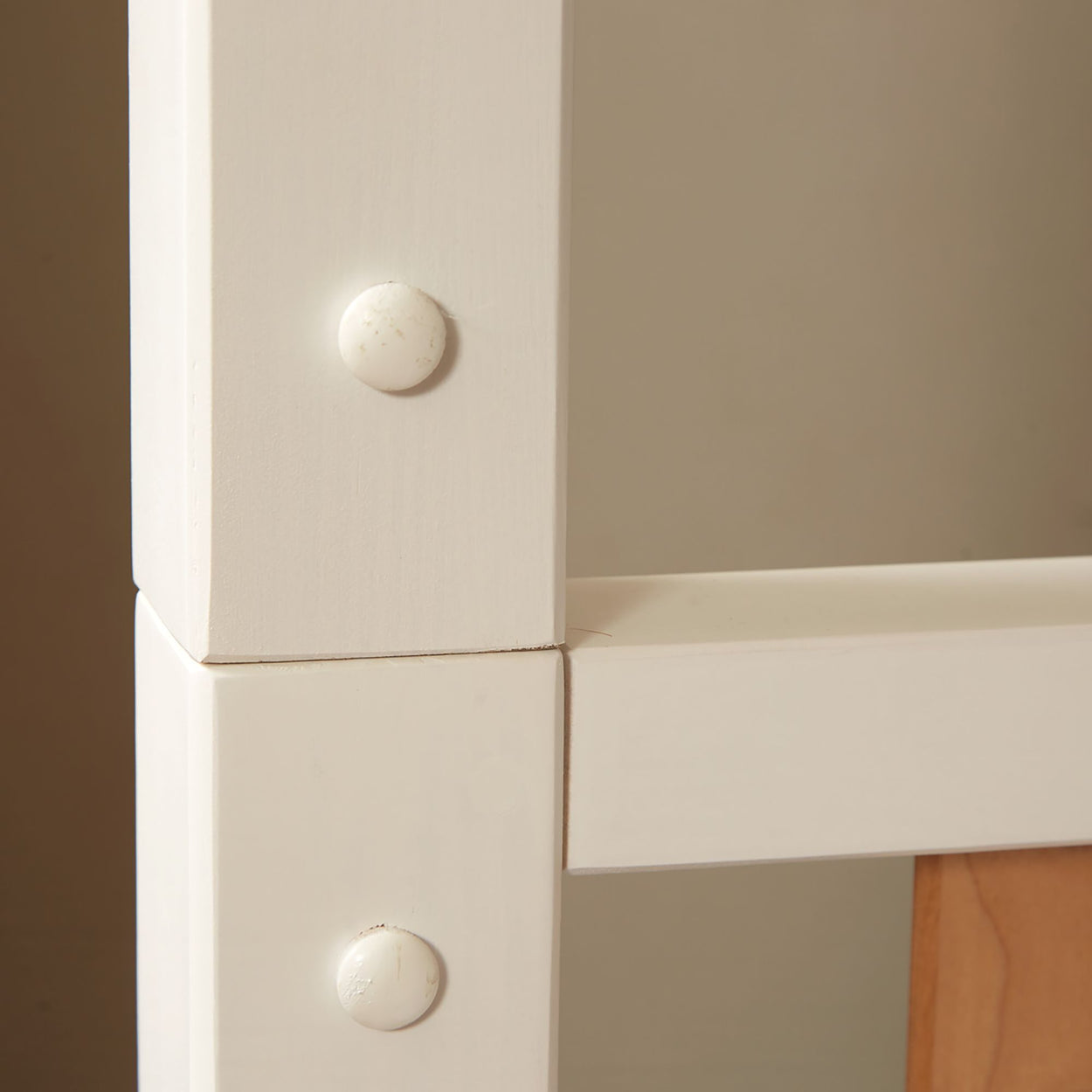 Close-up of wooden furniture joint with visible screws on a white bed frame.
