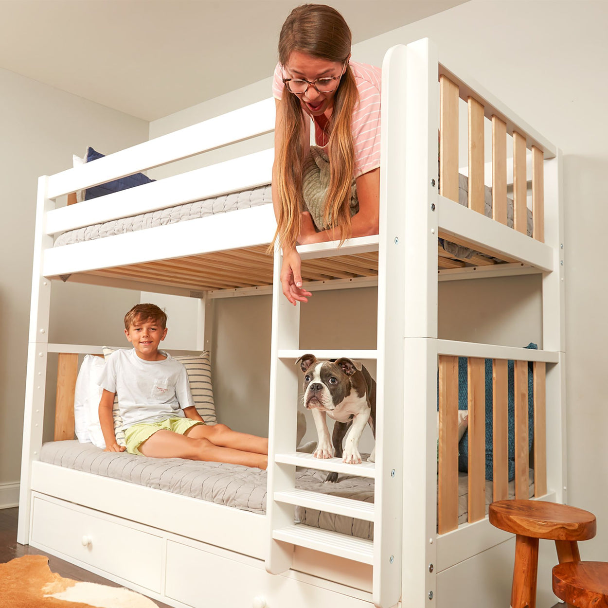 Woman and boy enjoying a white bunk bed with a dog on ladder in cozy bedroom.