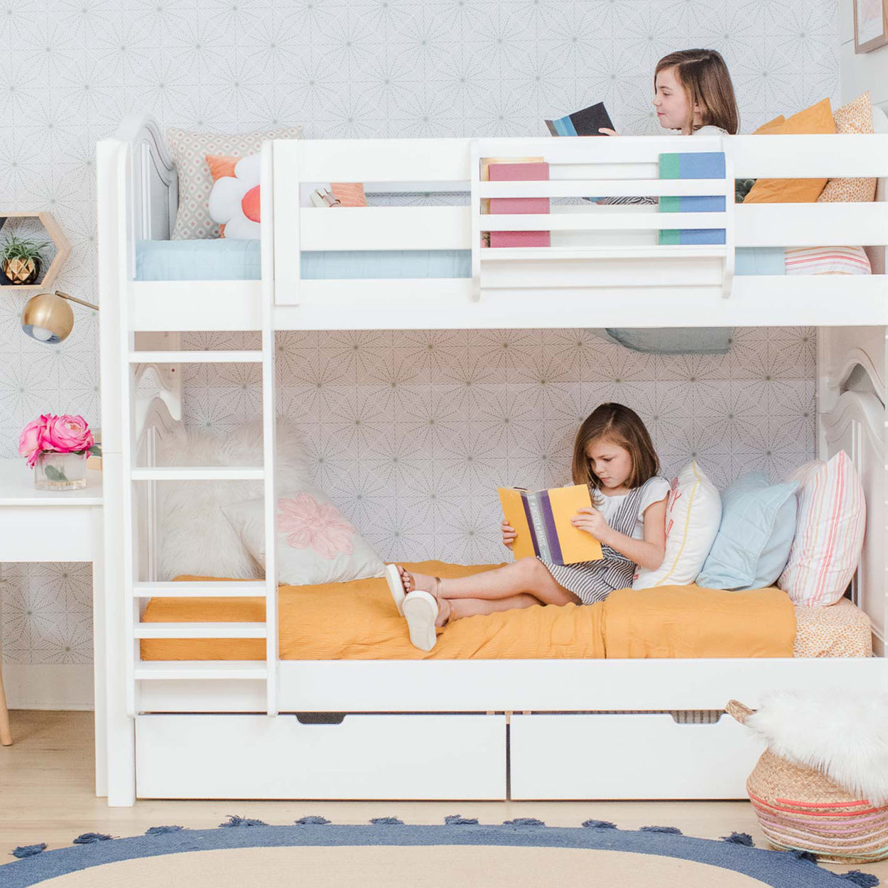 Children reading books on a white bunk bed with colorful pillows and modern room decor.