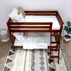 Wooden bunk bed with white bedding and decorative pillows in a cozy bedroom setting with a patterned rug.