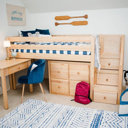 Light wood loft bed with built-in drawers and stairs, blue-striped bedding, navy velvet desk chair, study desk and red backpack in nautical kids' bedroom