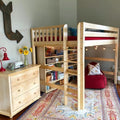 Kids wooden loft bed with built-in bookshelves and ladder, cozy reading nook with red beanbag, string lights, boho area rug and natural wood dresser with sunflowers
