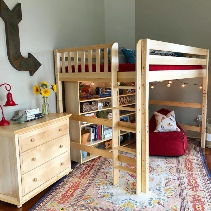Kids wooden loft bed with built-in bookshelves and ladder, cozy reading nook with red beanbag, string lights, boho area rug and natural wood dresser with sunflowers