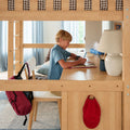 Child doing homework at a light-wood loft bunk bed with built-in study desk, lamp, backpack and school supplies in a bright kids' bedroom