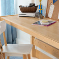 Home desk setup with light wood desk and white chair, Xbox console and controllers in a wicker basket, notebooks and corkboard
