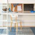 Kids homework station under loft bed: white desk and chair with corkboard, gold trophy and medal, chalkboard math, notebooks and blue lunchbox.
