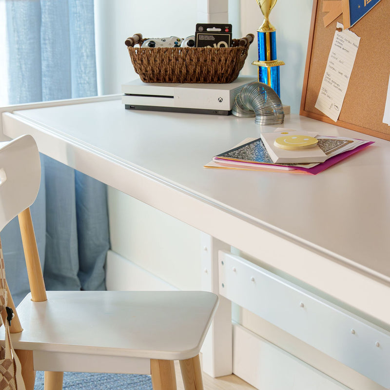 Organized kids' study and gaming desk: white desk with Xbox console and controllers in a wicker basket, blue trophy, stacked notebooks and corkboard