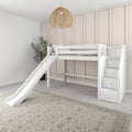 White wooden loft bed with slide and stair-storage in neutral kids room featuring a rattan pendant light, board-and-batten accent wall, beige rug and plant