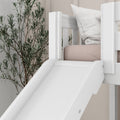 White wooden indoor slide attached to a children's loft bed in a modern kids' bedroom with blush-pink mattress, white pillow, and botanical wall mural