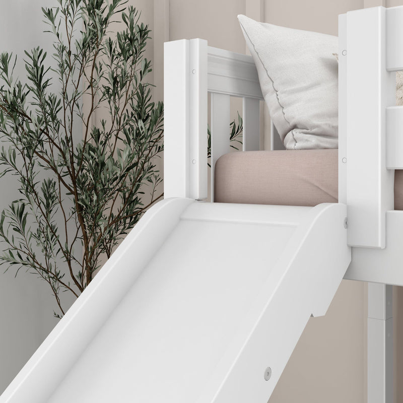 White wooden indoor slide attached to a children's loft bed in a modern kids' bedroom with blush-pink mattress, white pillow, and botanical wall mural