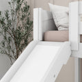 White wooden children's bunk bed with slide, blush mattress and white pillow in a neutral nursery with tall indoor plant