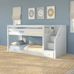 White twin-over-twin bunk bed with staircase storage drawers in a coastal blue kids' bedroom with striped yellow-and-blue bedding, framed nautical wall art, and woven jute rug