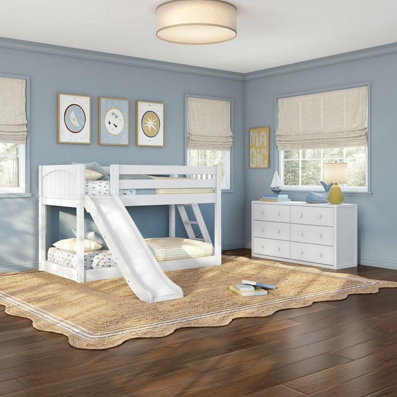Children's bedroom with white bunk bed and slide, light blue walls, woven jute rug, white dresser, lamp and nautical wall art by windows with Roman shades