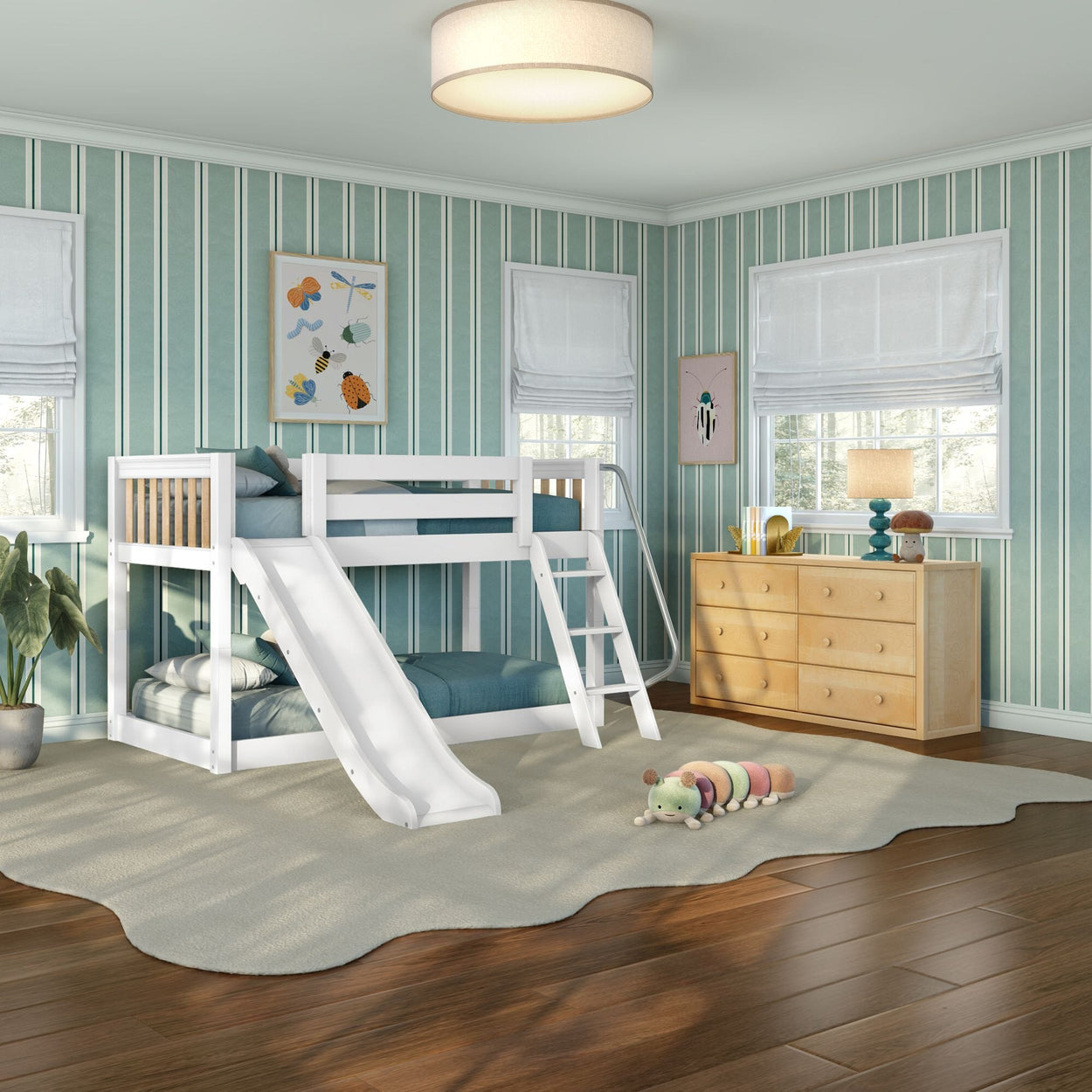 White bunk bed with slide in a modern kids' bedroom with teal striped wallpaper, wooden dresser, hardwood floors and plush caterpillar toy