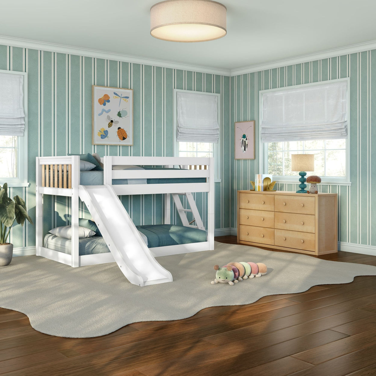 Bright kids bedroom with white twin bunk bed and slide, turquoise striped wallpaper, wooden dresser, beige area rug, plush caterpillar toy, framed insect art and natural light from windows