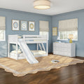 White bunk bed with slide in a blue children's bedroom featuring a natural jute rug, white dresser, lamp, toy whale and window roman shades