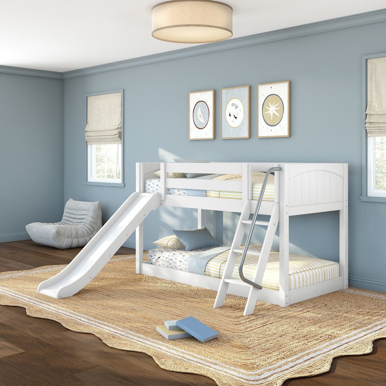 White wooden twin-over-twin bunk bed with slide and ladder in a modern blue kids' bedroom with striped bedding, natural jute rug, cozy lounge chair, and framed wall art.