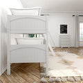 White wooden bunk bed with ladder and quilted pillows in a minimalist kids bedroom with neutral tassel rug, dresser and herringbone wood floor