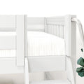 White wooden bunk bed corner with ladder, safety guardrail and twin mattress in a bright children's bedroom with potted plant