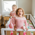 Two toddlers in striped pajamas playing in a white wooden crib in a bright nursery, joyful children at play