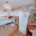 White loft bunk bed in charming boho kids bedroom with floral wallpaper, rattan hanging chair, cozy rugs and whimsical decor
