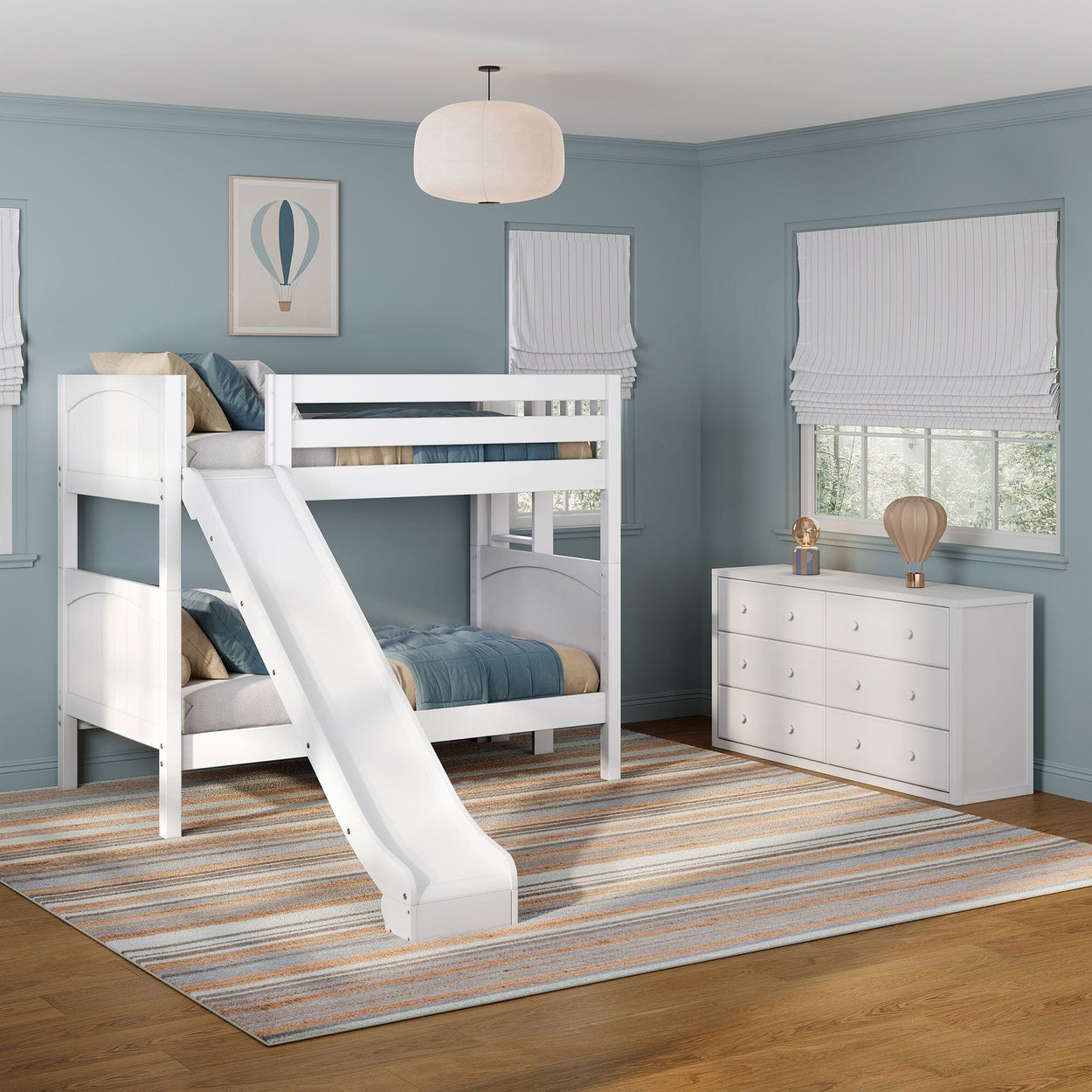 White wooden bunk bed with slide in blue kids' bedroom featuring a striped area rug, white dresser, Roman shades and hot air balloon wall art