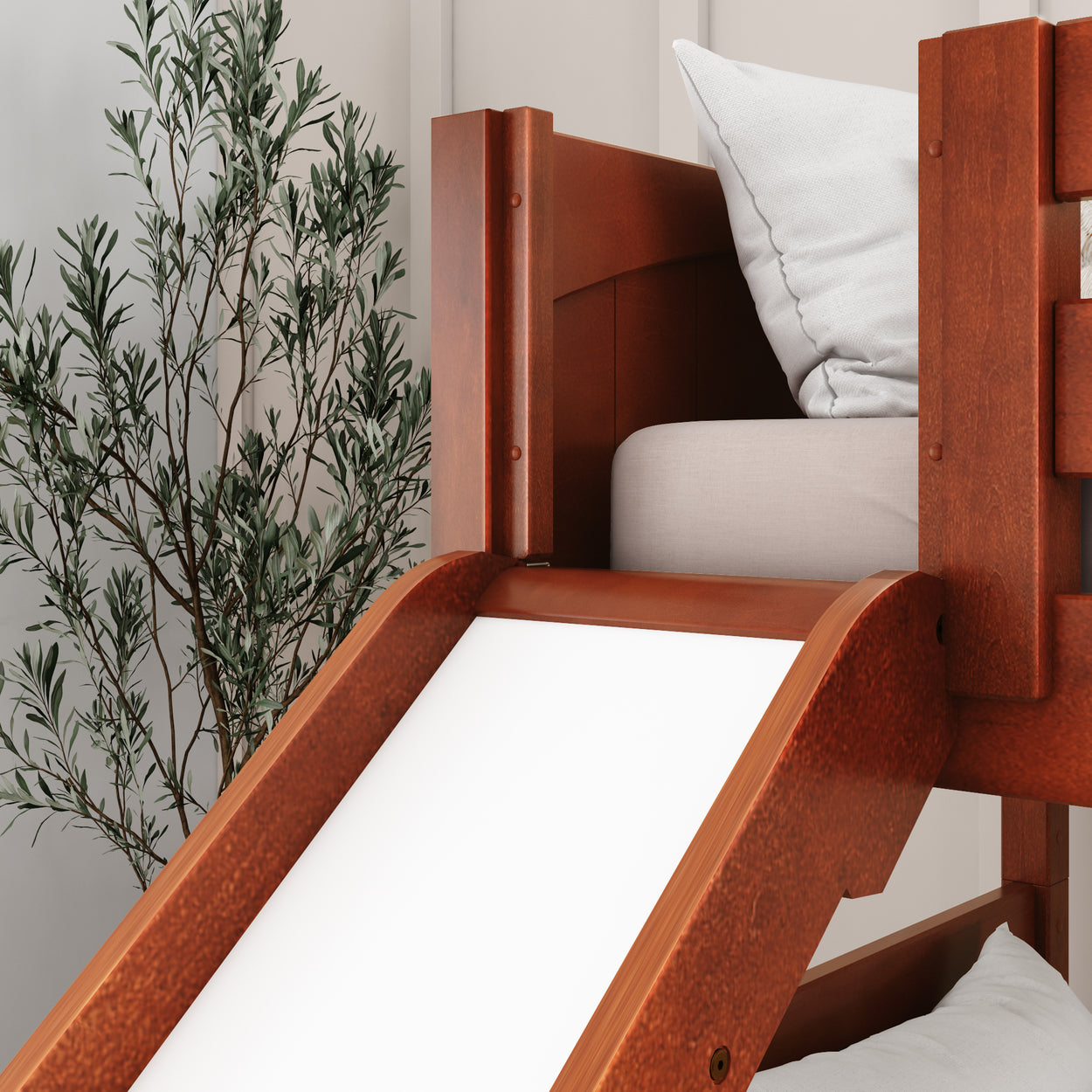 Wooden bunk bed with slide and cozy cushion in a children's room with greenery decor.