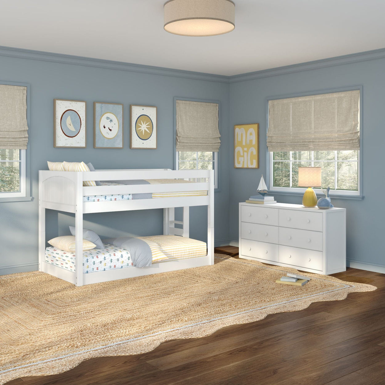 Kids' coastal-style bedroom with white twin-over-twin bunk bed, white six-drawer dresser, woven jute area rug on hardwood floors, blue painted walls, nautical wall art, linen Roman shades and table lamp