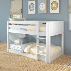 White wooden twin-over-twin bunk bed with built-in ladder and guardrails in a coastal blue kids bedroom, yellow striped bedding, moon and star wall art, and woven jute rug