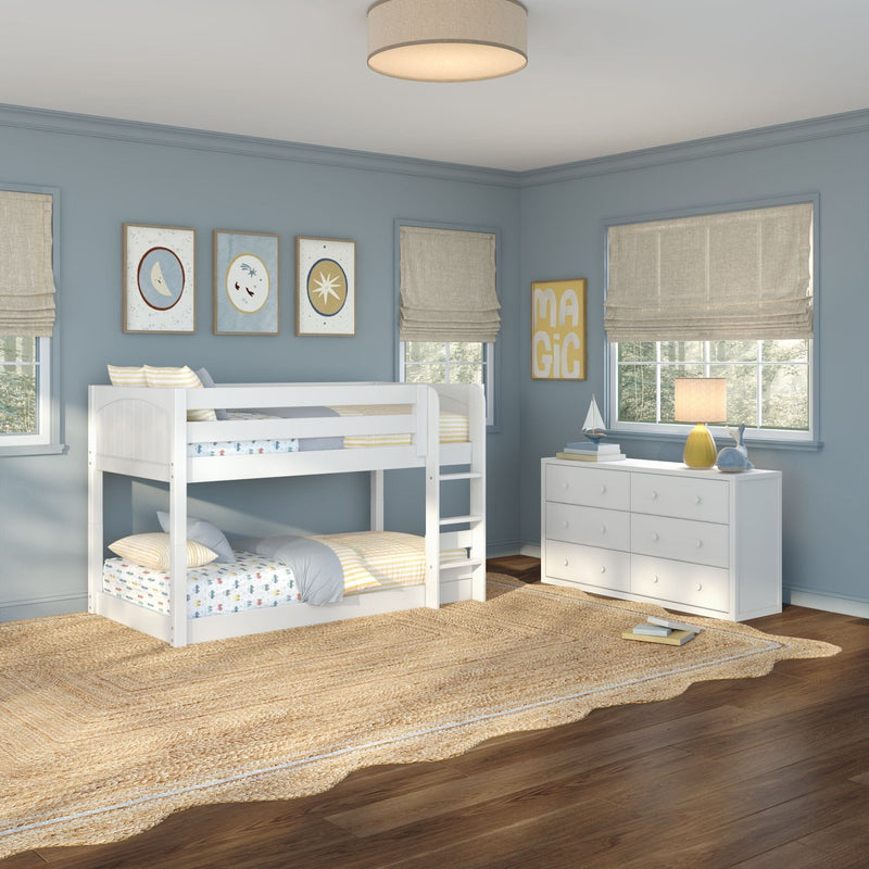 Modern children's bedroom with white bunk bed, light blue walls, beige Roman shades, white dresser, woven jute rug, framed wall art and bedside lamp